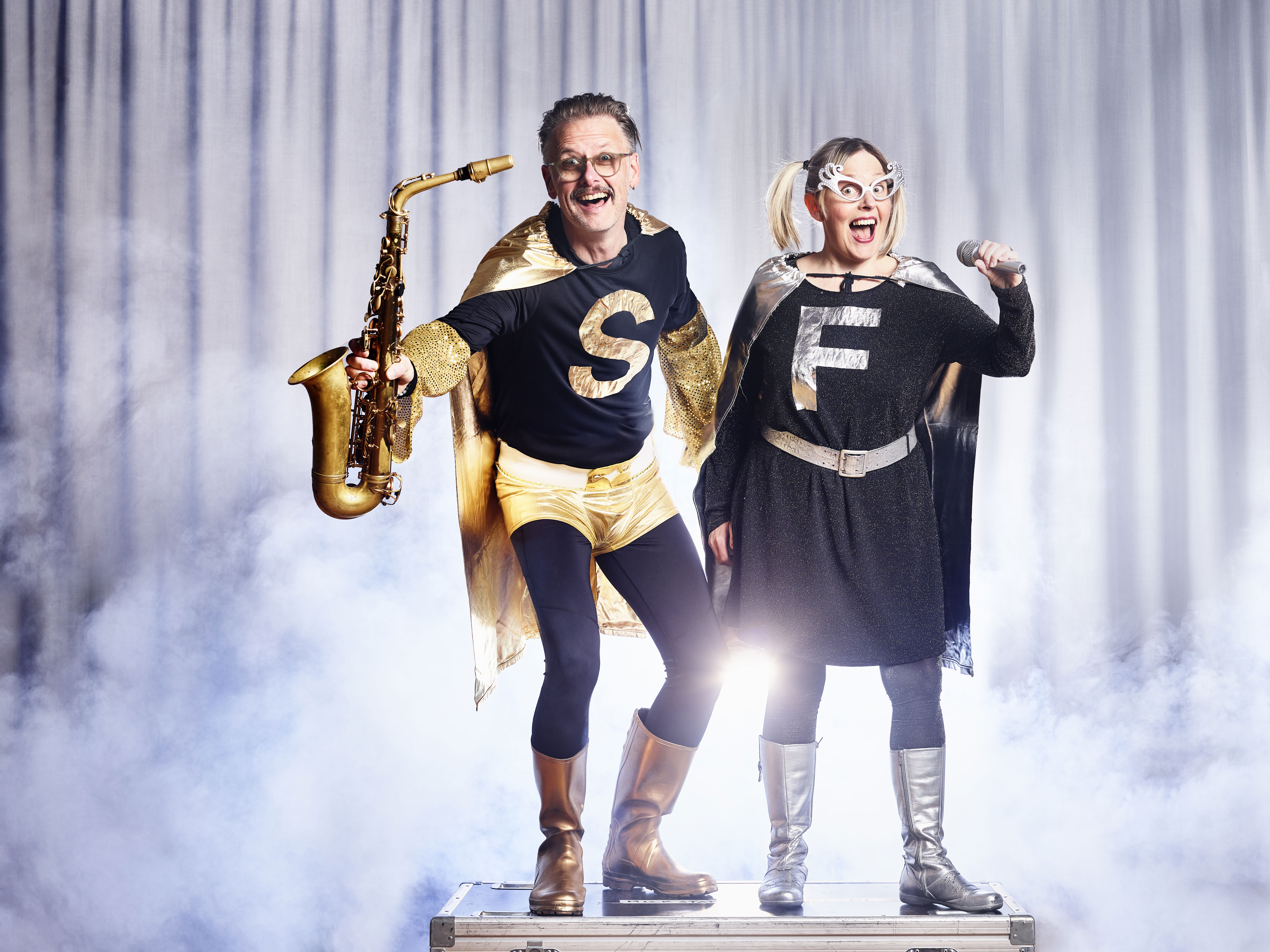 Musikhjältarna står med saxofon och mikrofon i rök och motljus.  